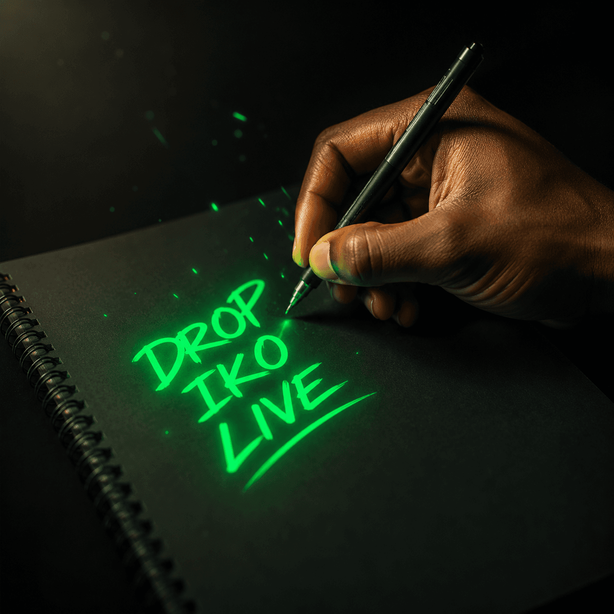 A creator handwriting DROP IKO LIVE in glowing green on a black sketchpad