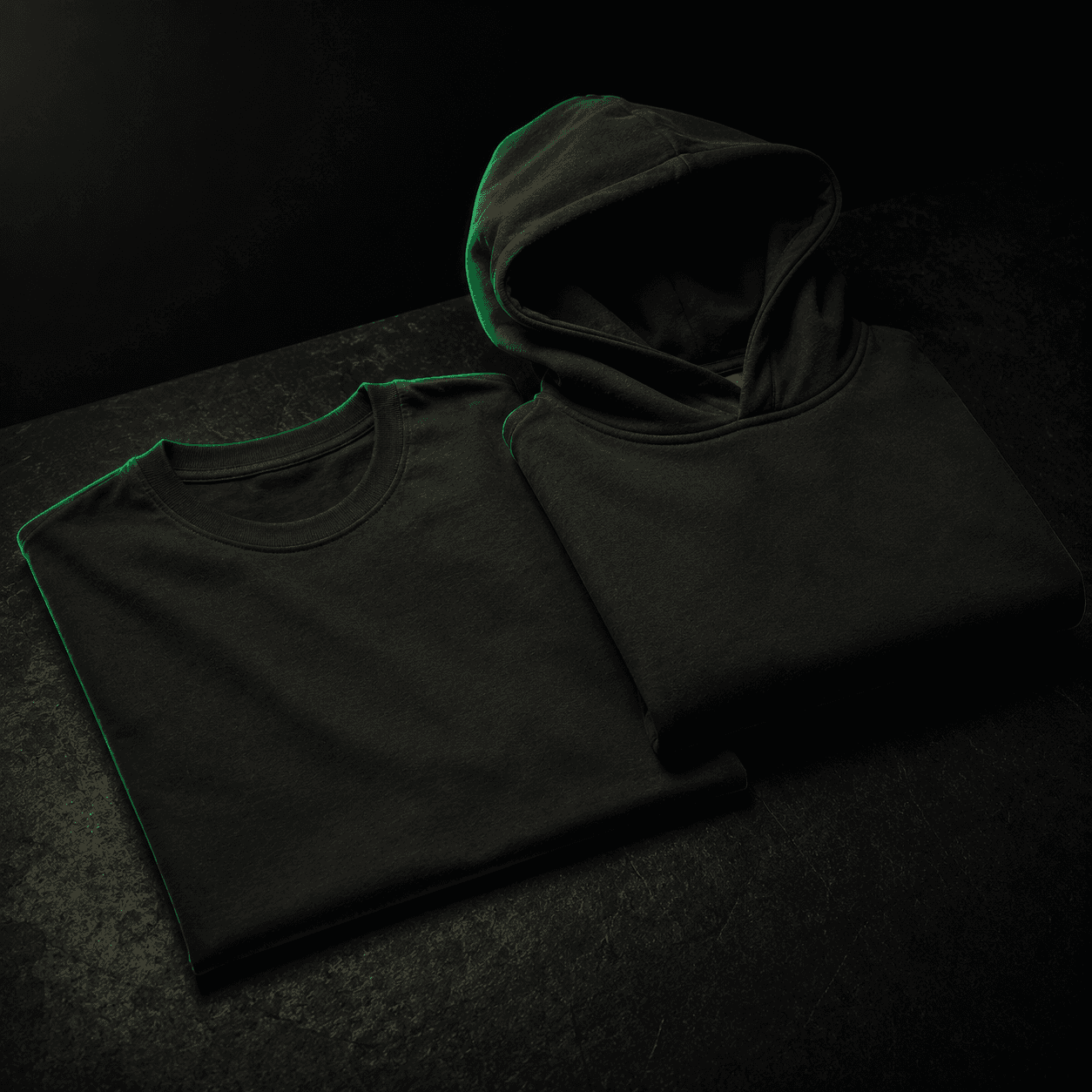 A premium folded black tee and streetwear hoodie on a dark surface