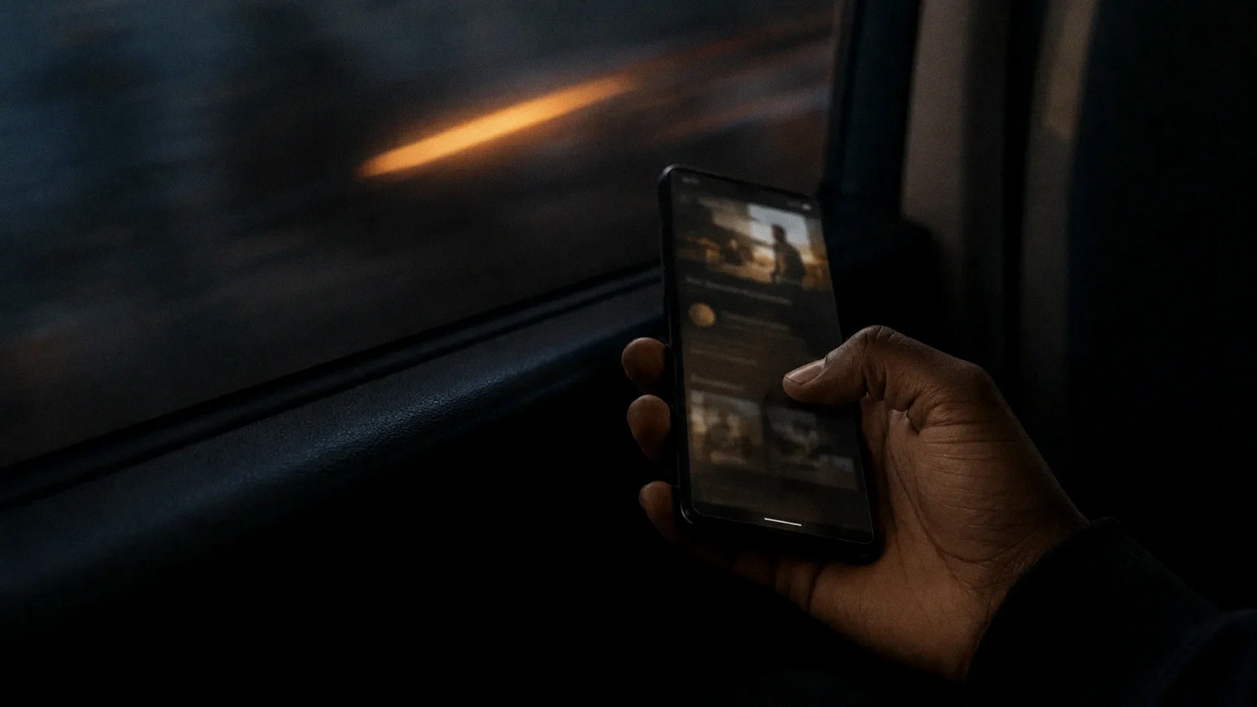 A hand holding a phone in the back of a matatu at dusk, orders scrolling past the window blur