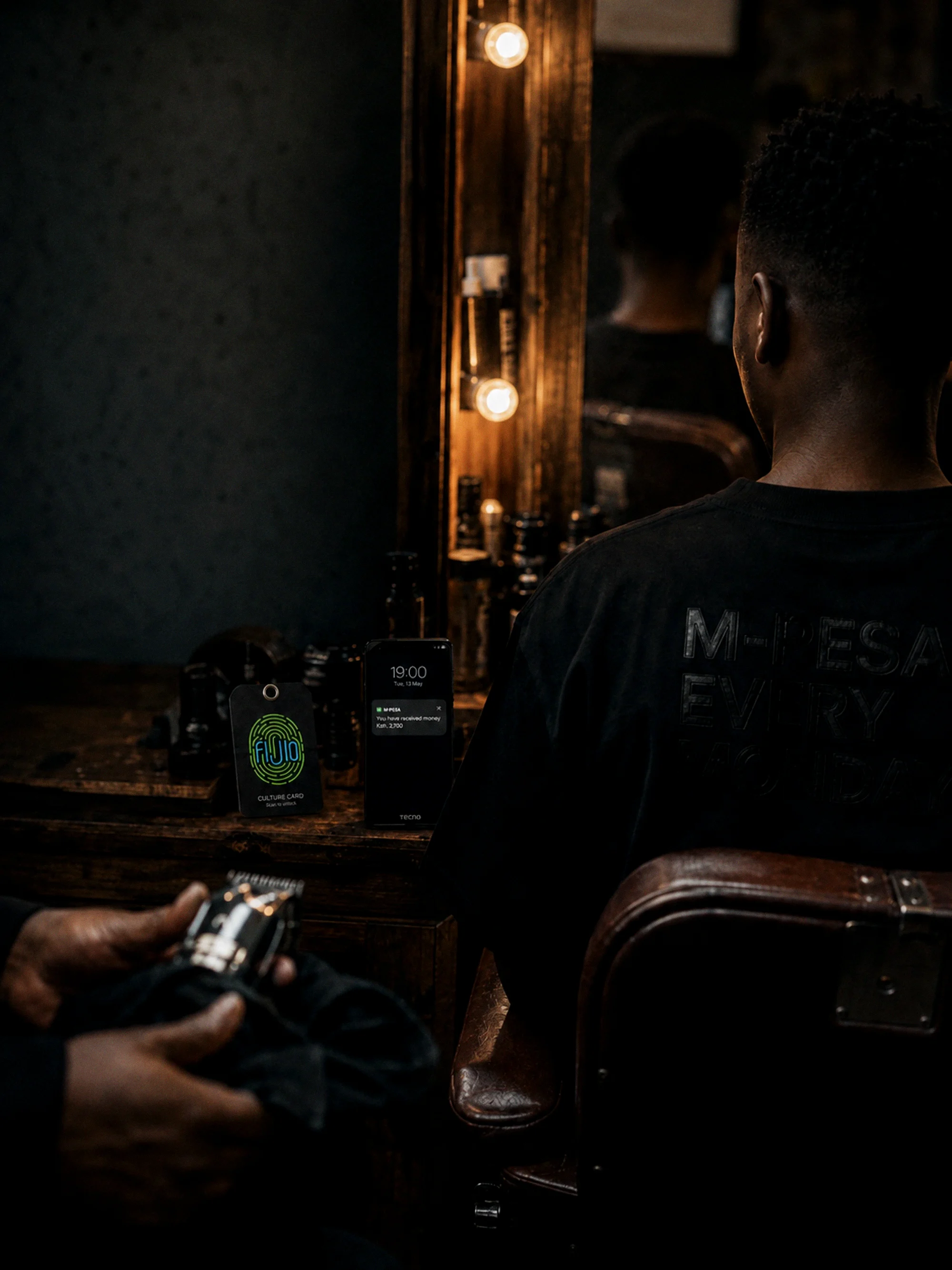 A kinyozi mirror, a phone payment notification glowing at 19:00
