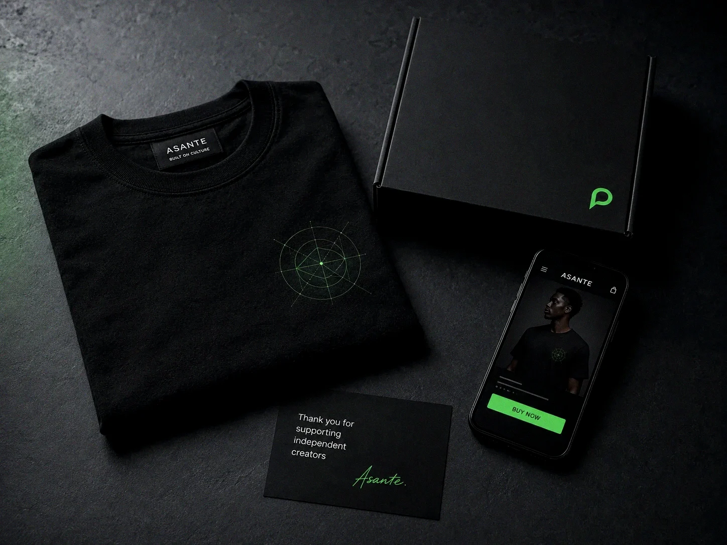 Launch Drop: folded black tee, plain box and a thank-you card beside a phone showing the storefront