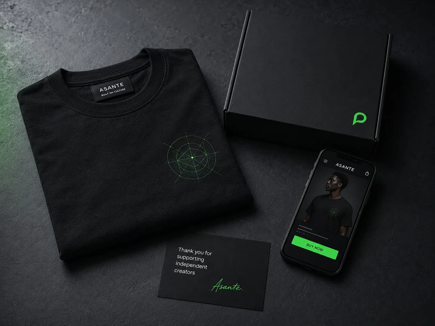 Launch Drop: folded black tee, plain box and a thank-you card beside a phone showing the storefront